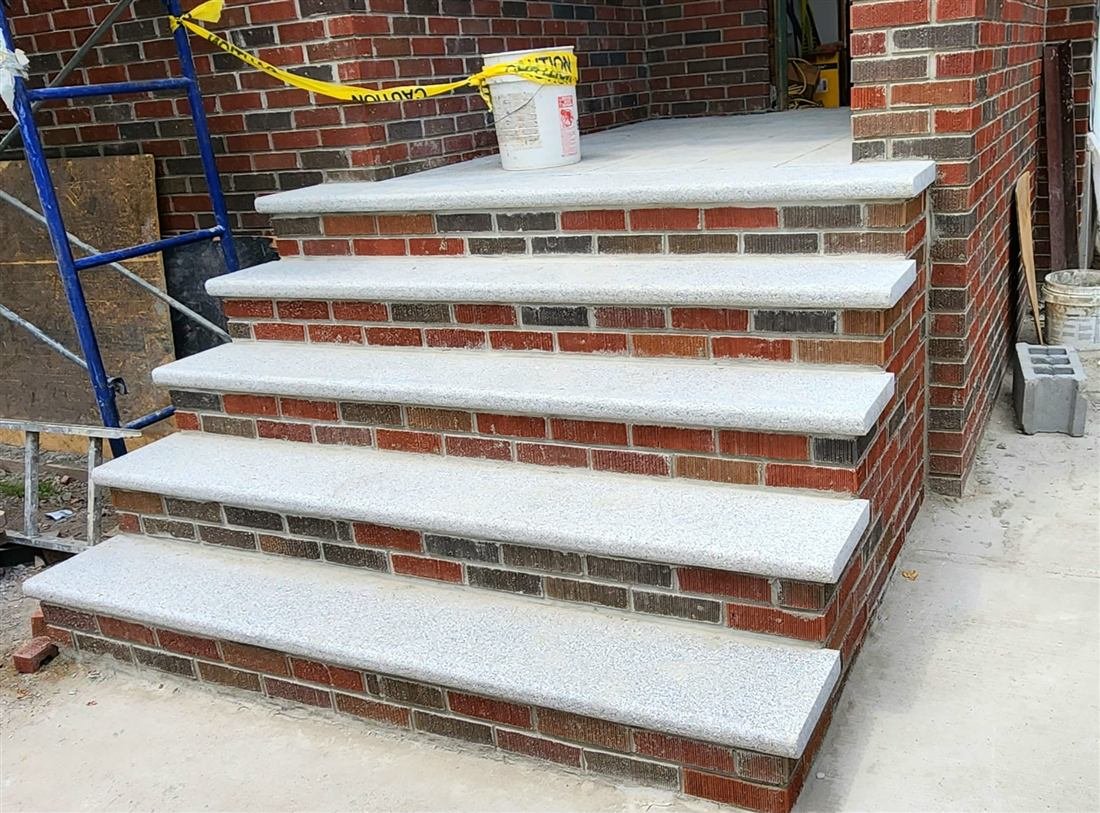 Newly built brick entry steps with granite/bluestone treads at a residential brick facade, caution tape, scaffold frame and construction materials still on site.