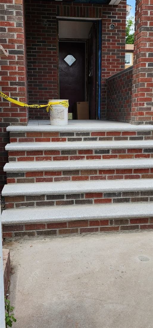 Sharp photo of newly rebuilt brick porch steps with fresh granite treads at a residential home entrance, caution tape and a mortar bucket still on site indicating work just completed.