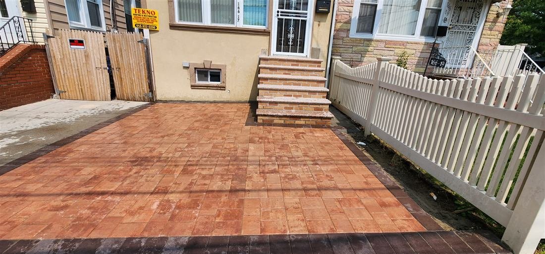 Real finished-project photo of a residential front yard in Queens-style attached housing: new terracotta paver patio with dark brick border, rebuilt brick-and-stone entry steps, and a yellow Tekno Roofing & Restoration jobsite sign on the fence — sharp, well-lit, strong before/after appeal.