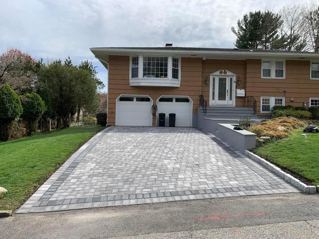 Second angle of the same completed paver driveway project showing the full apron, border detail, retaining/planter wall and cobblestone edging at the residential home.