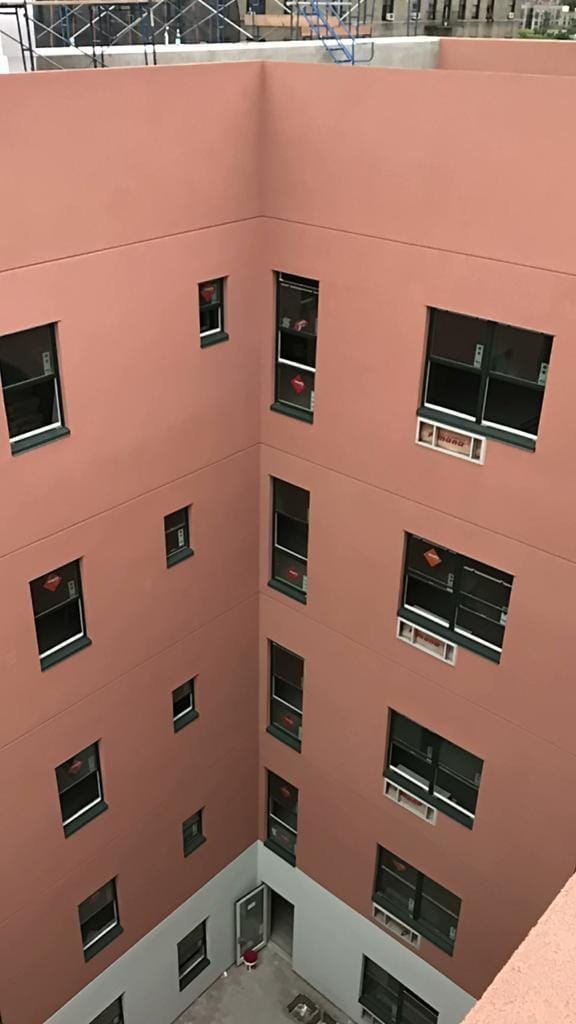 Downward view into the interior courtyard of a multi-story residential building with freshly applied salmon-pink stucco and new windows still carrying manufacturer stickers.