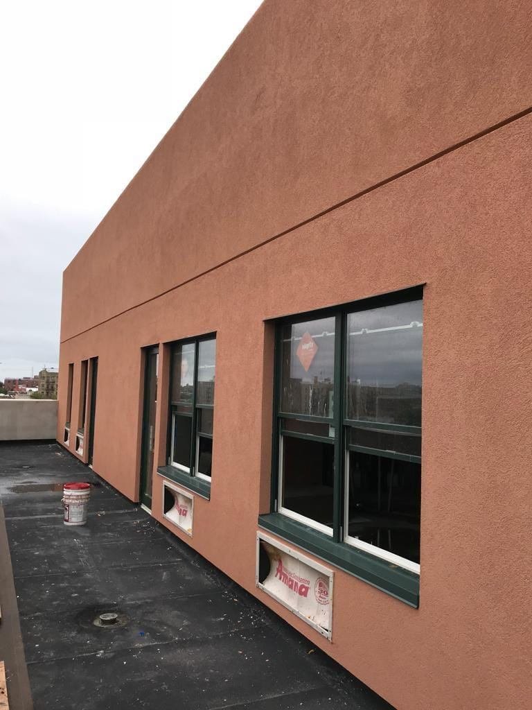 Upper-floor setback of a commercial building with freshly completed terracotta stucco and new green-framed windows, shot from the flat roof; overcast light.
